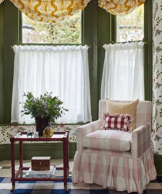 Colorful living room, yellow blinds, green painted walls, pink and white checkered armchair, floral wallpaper, blue patterned rug